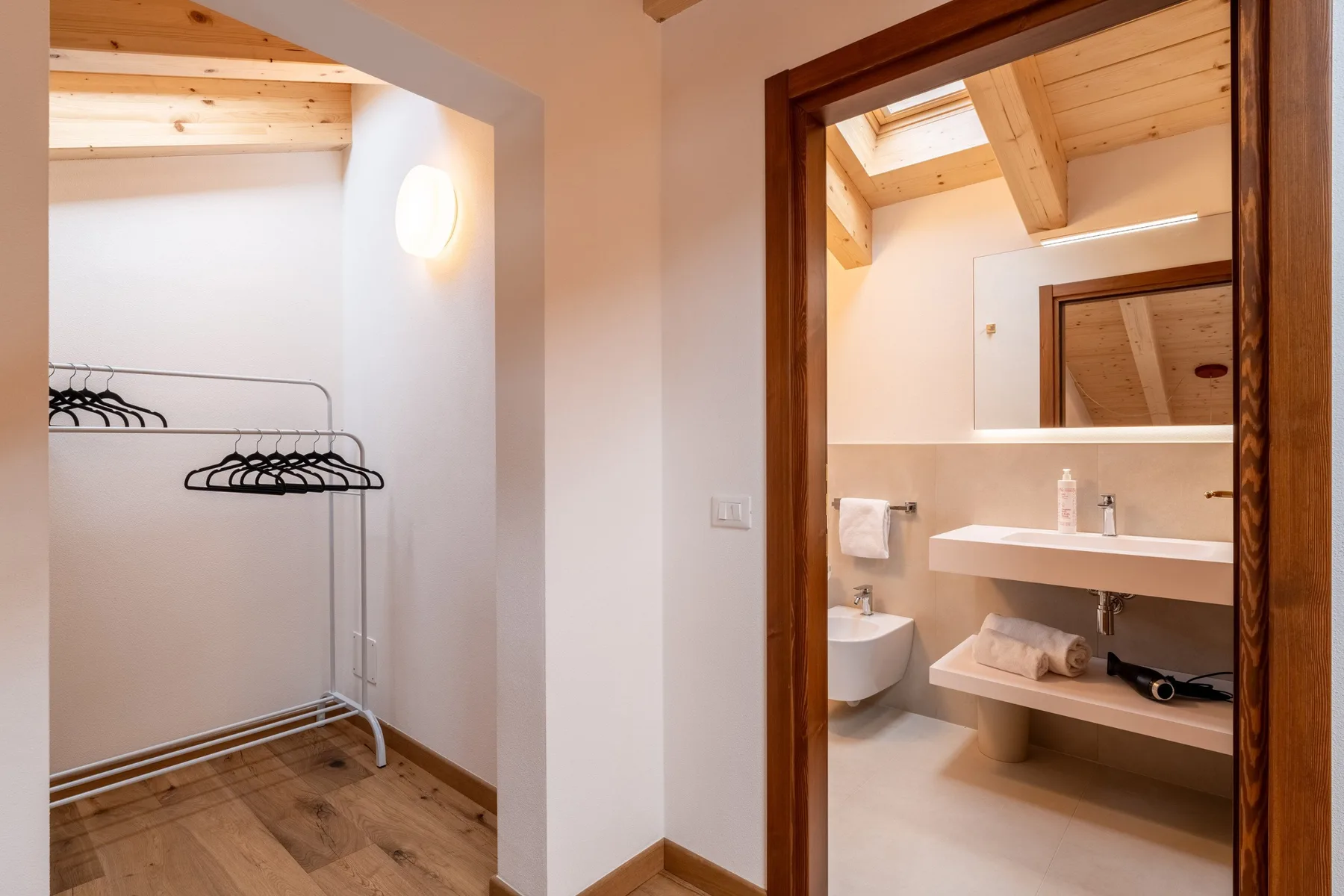 A bathroom with a wall-mounted sink and an adjoining clothes rack.