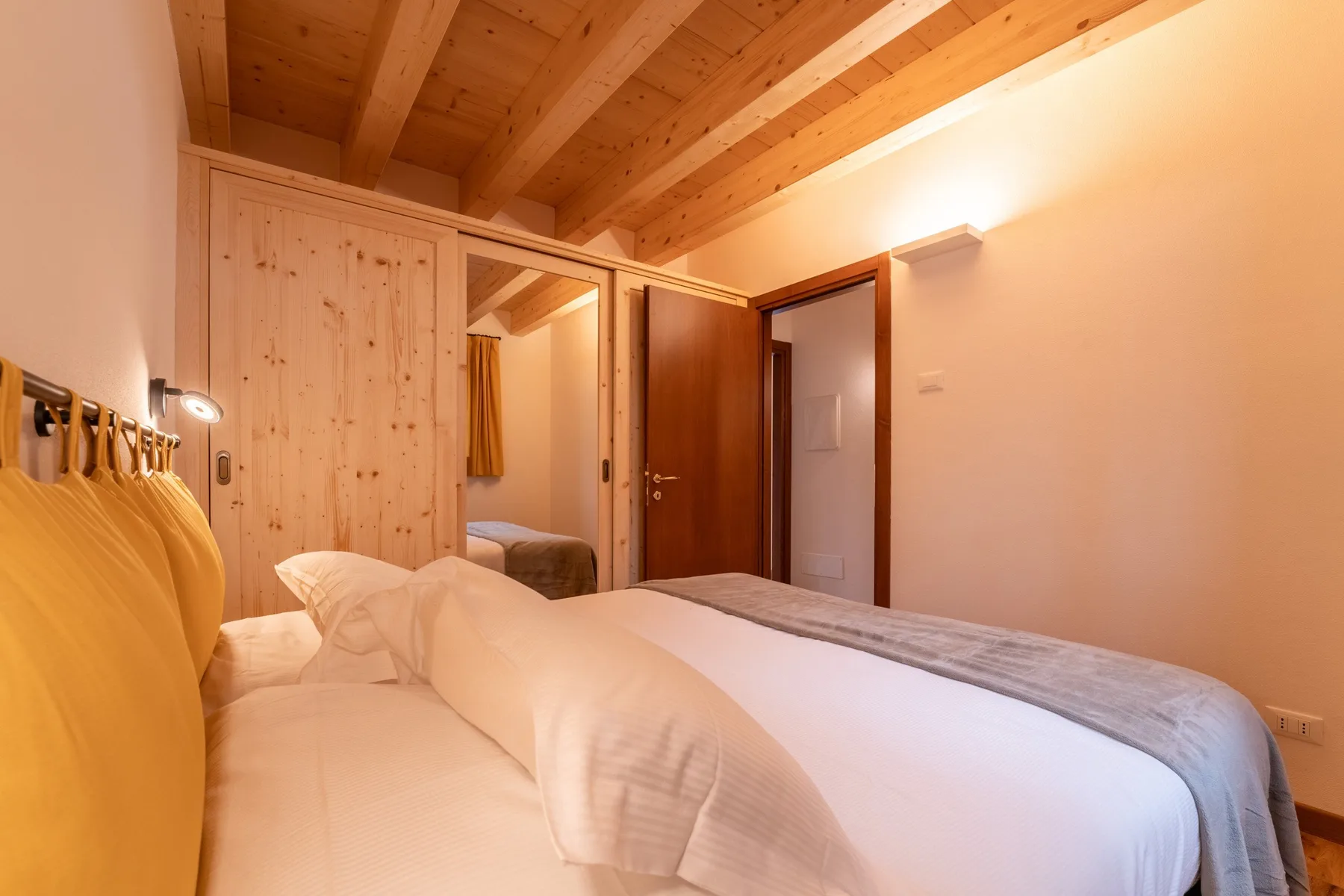 A bedroom with beds beneath a sloped wooden ceiling and a mirrored wardrobe.
