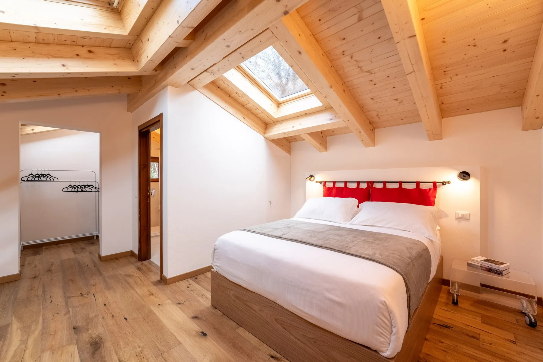 A bedroom with a bed beneath a sloped wooden ceiling and skylight.