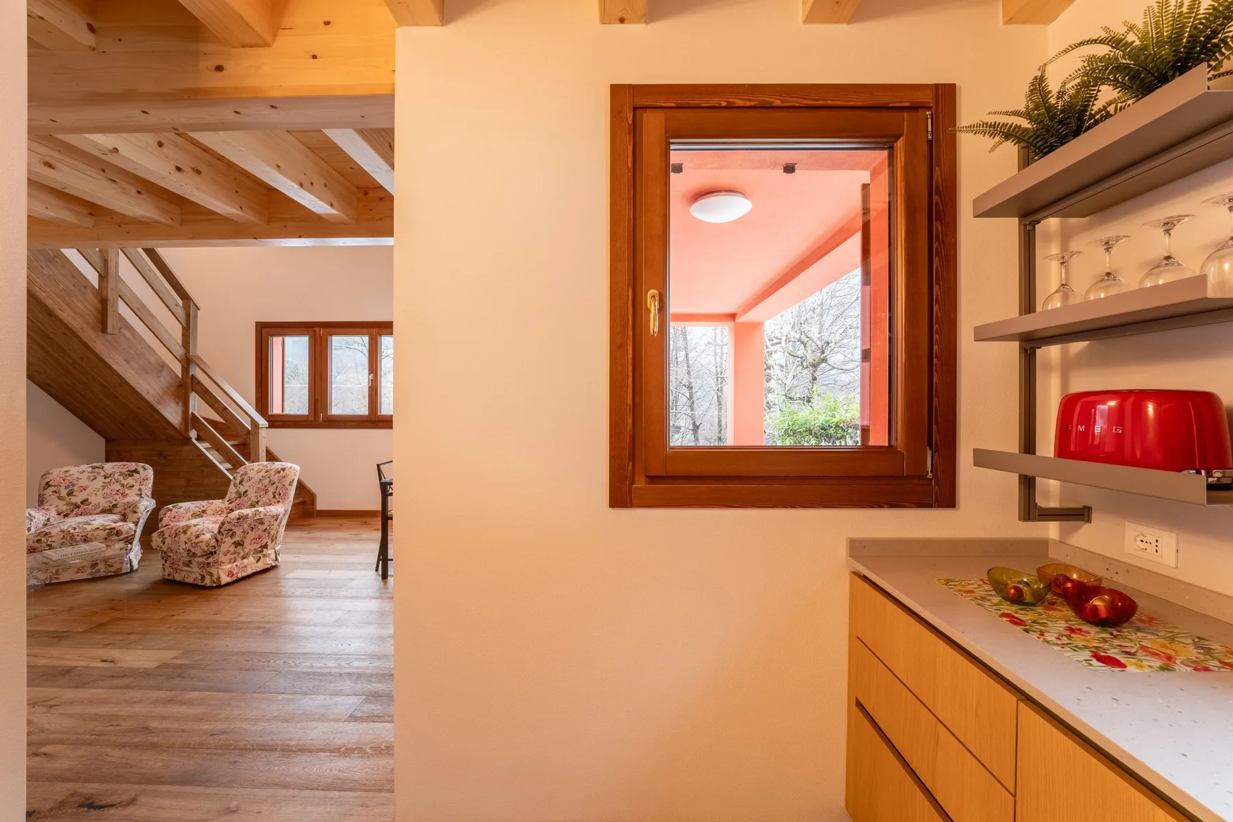 A wood-paneled kitchen counter and window overlook a living area with seating.