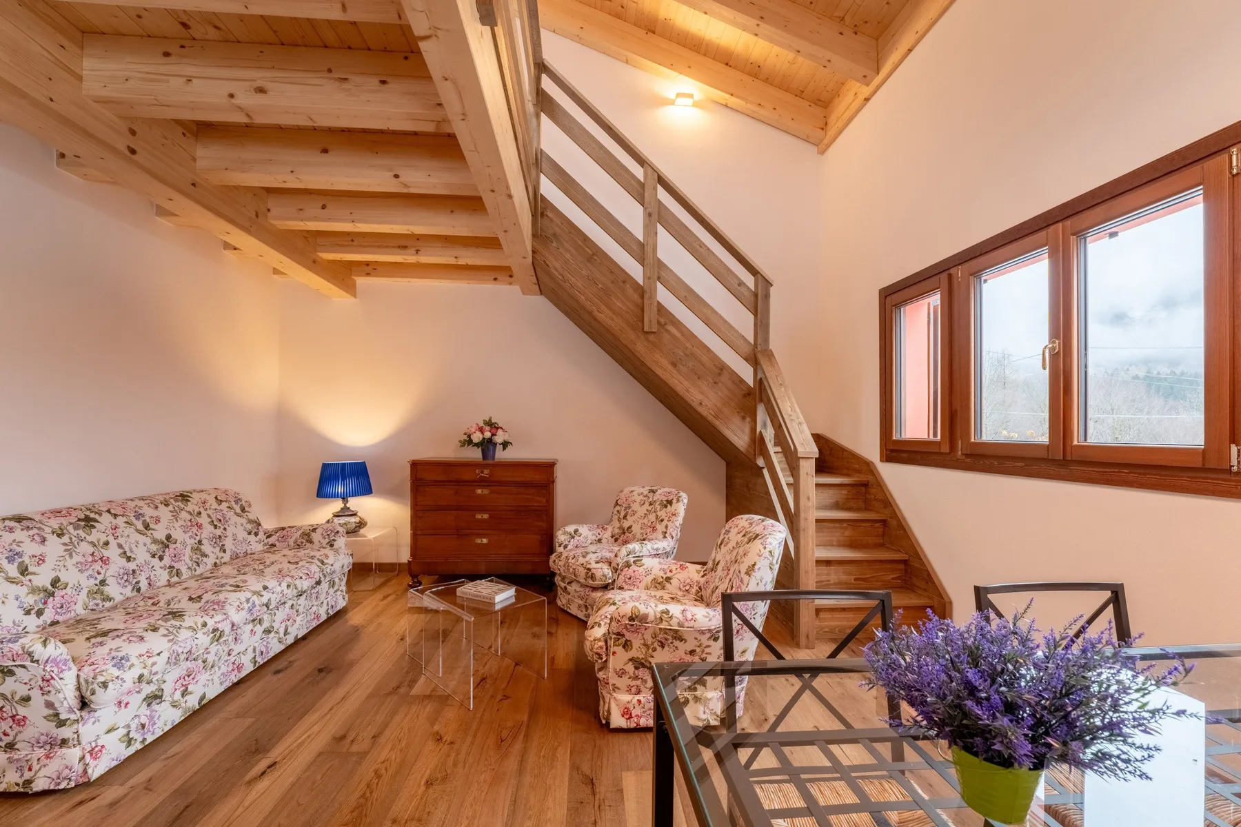A bright living room with floral seating beneath a wooden staircase.