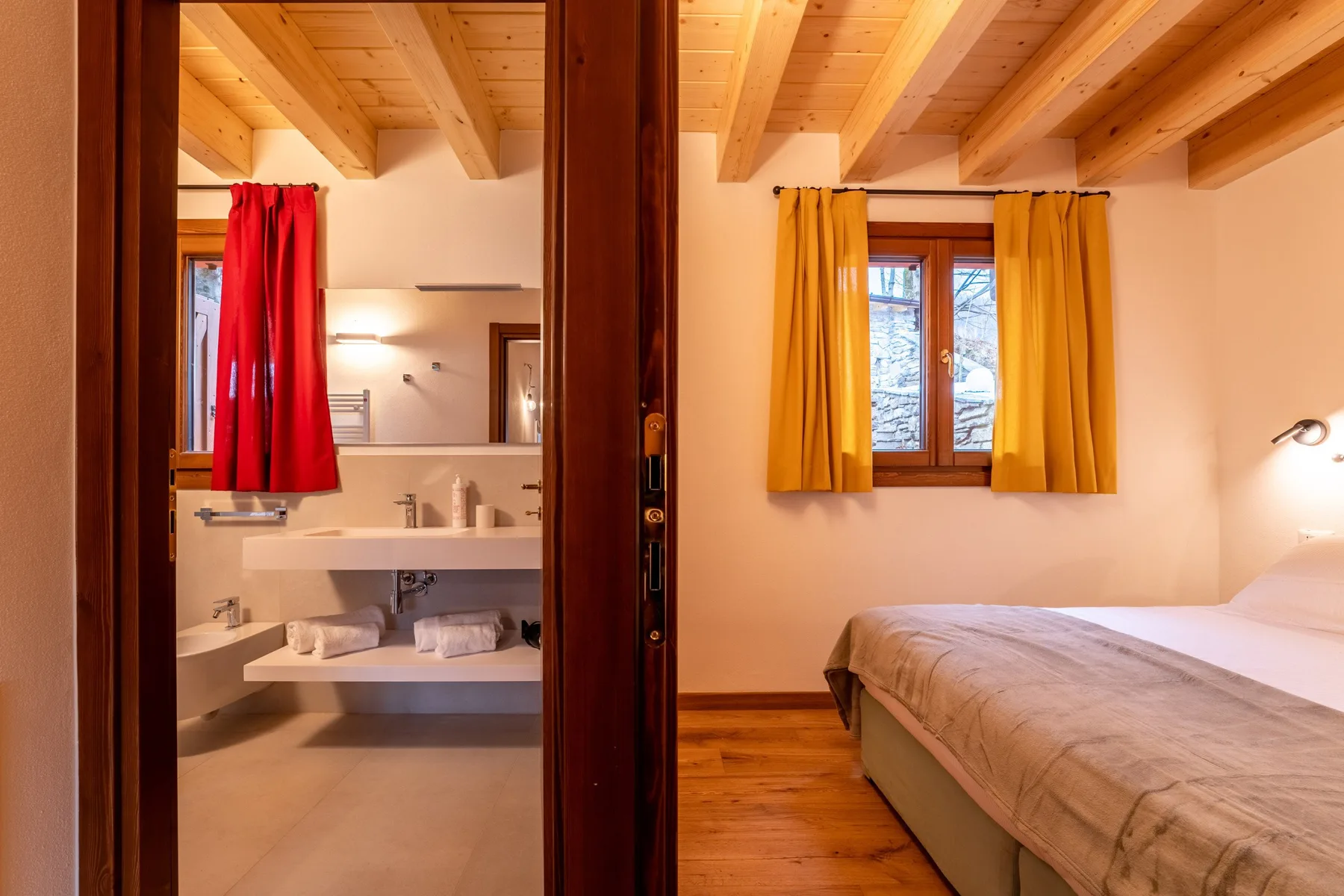 A bedroom with a bed beside a bathroom visible through an open doorway.