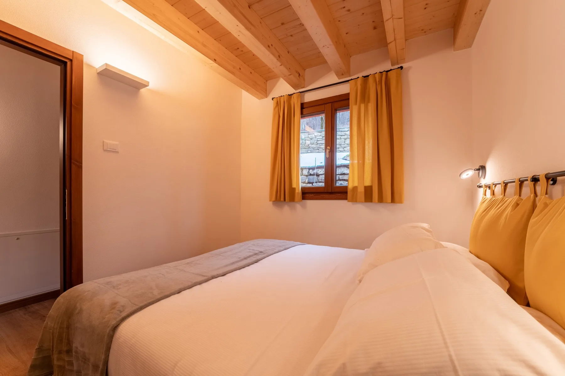 A bedroom with a bed beneath a sloped wooden ceiling and a curtained window.