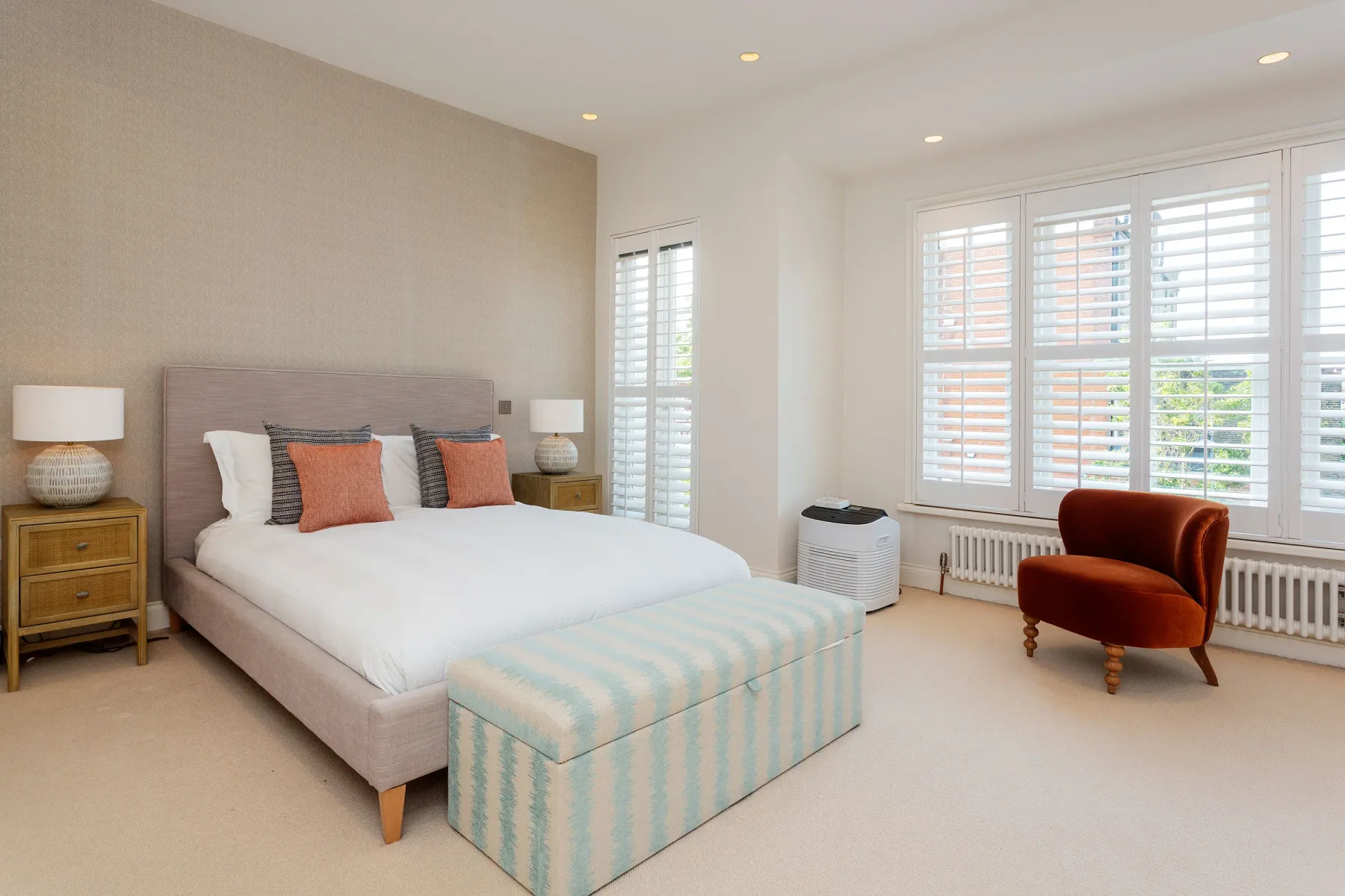 Un dormitorio luminoso con una cama grande y un banco tapizado a sus pies.