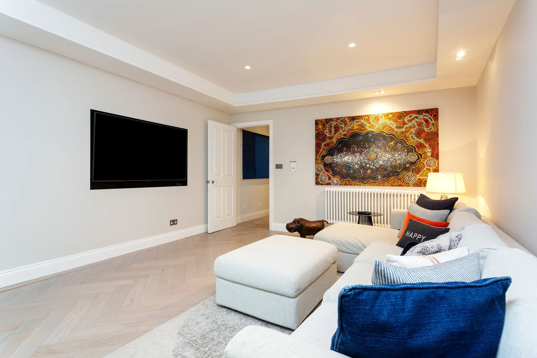 Una sala luminosa con sofá seccional, otomana y televisor montado en la pared.
