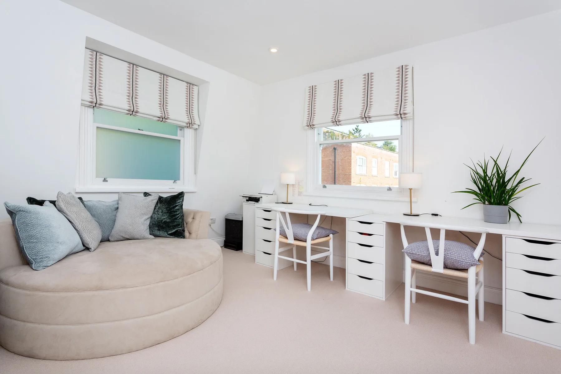 Una luminosa zona de estar y trabajo cuenta con un rincón de asiento redondeado y escritorios junto a las ventanas.