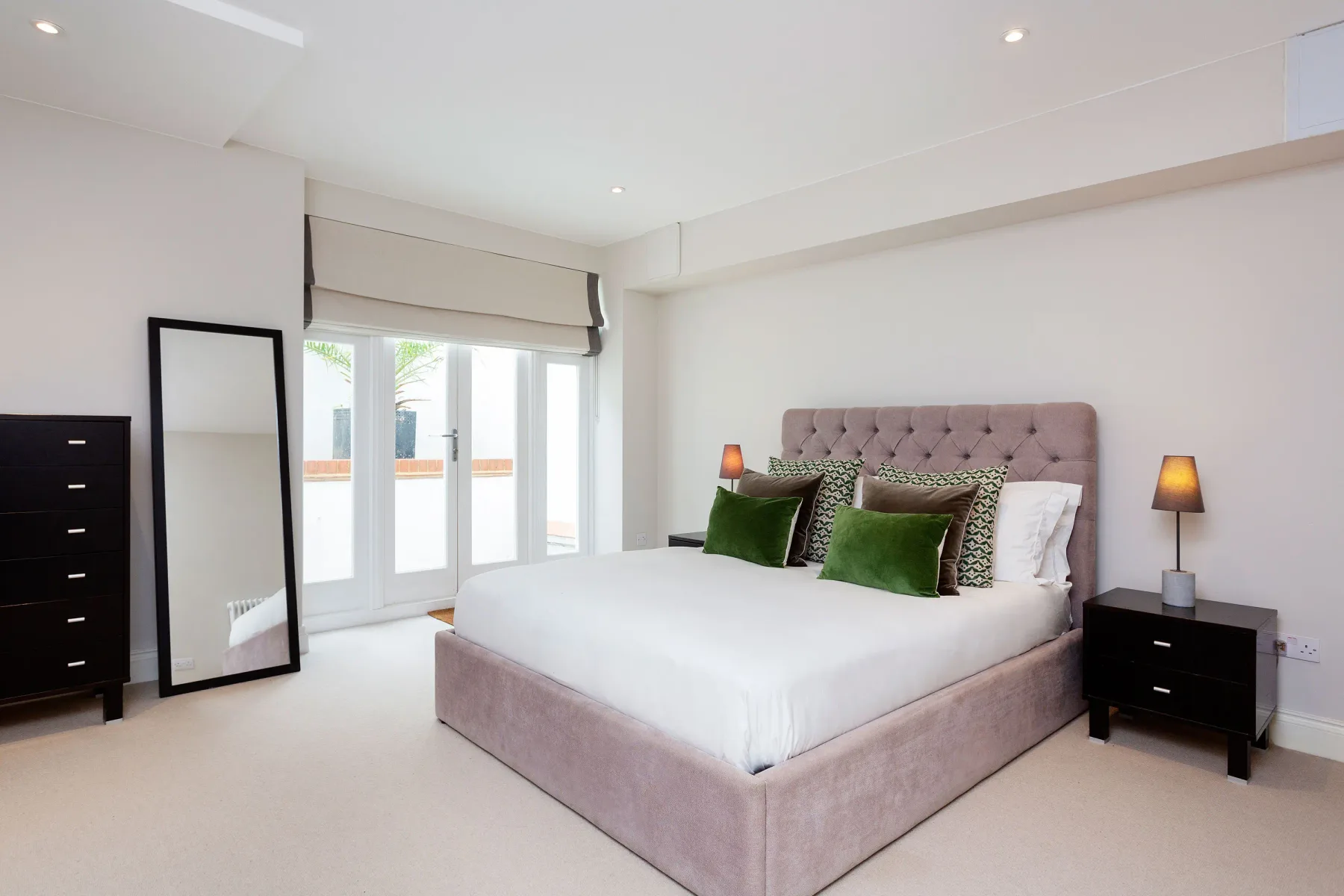 Un dormitorio luminoso con una cama grande y ventanas altas.
