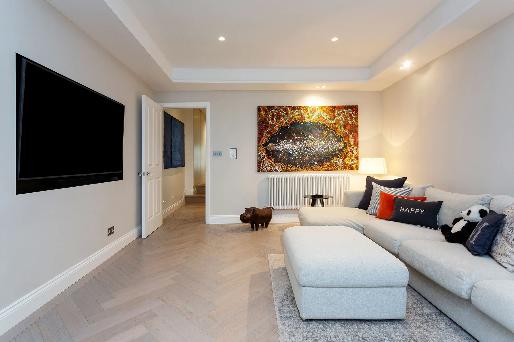 A bright living room with a large sectional sofa and colorful artwork above the radiator.