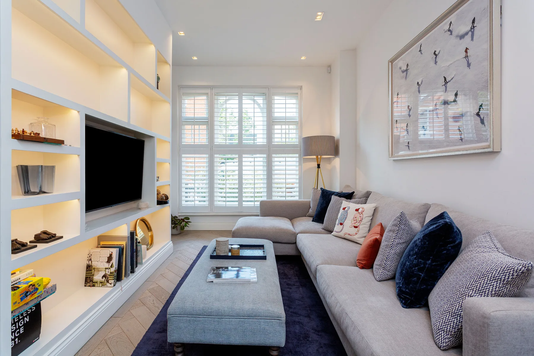 A bright living room with a sectional sofa, coffee table, and built-in media shelves.