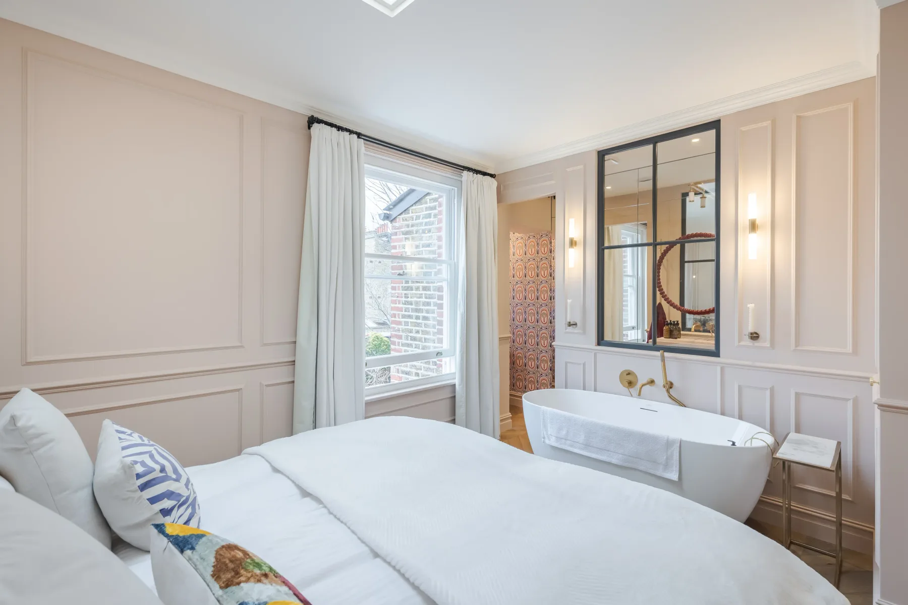 Un dormitorio con una cama junto a una bañera exenta y una ventana grande.