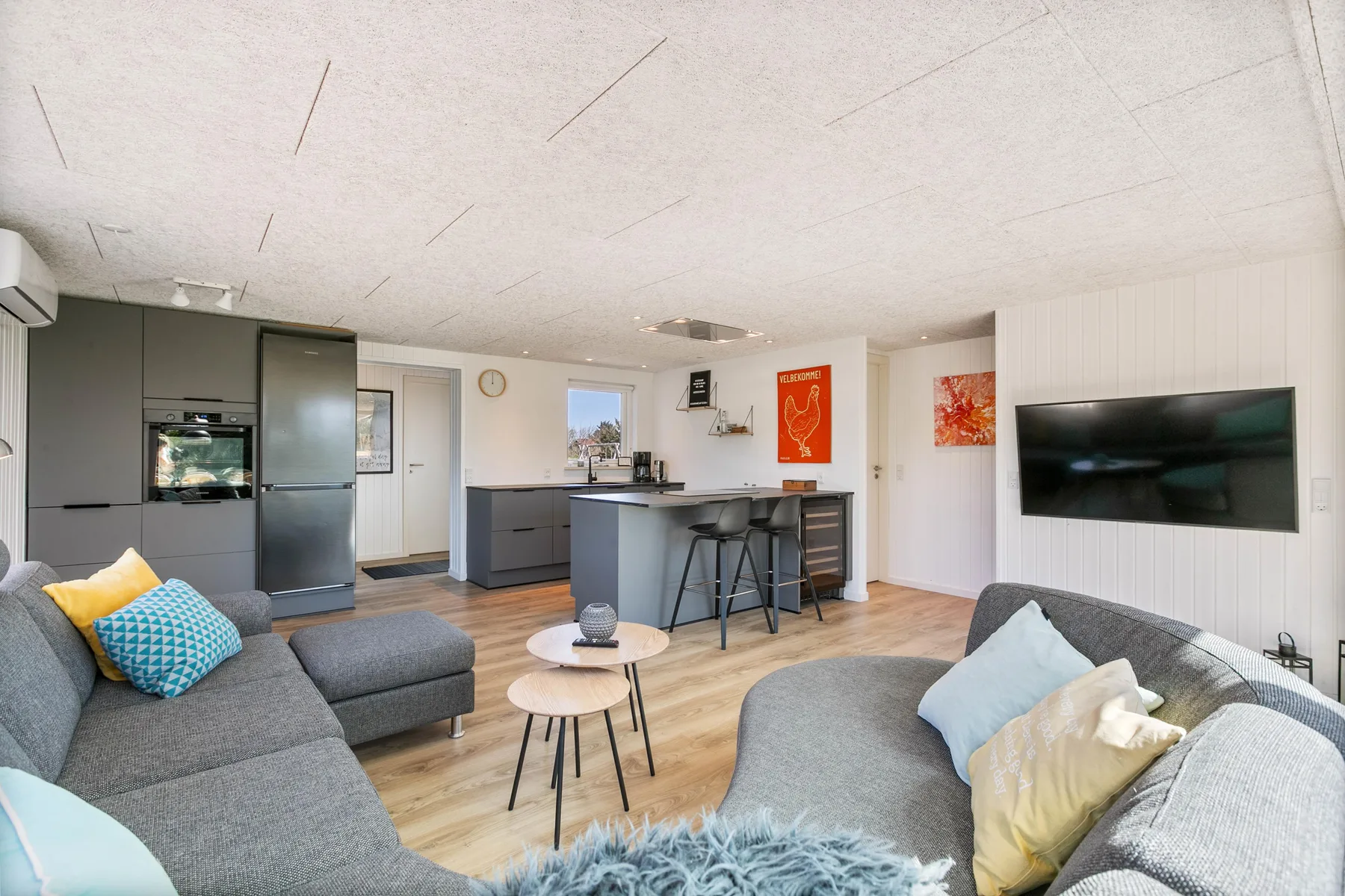Sala de estar y cocina de concepto abierto, con asientos grises y una barra.