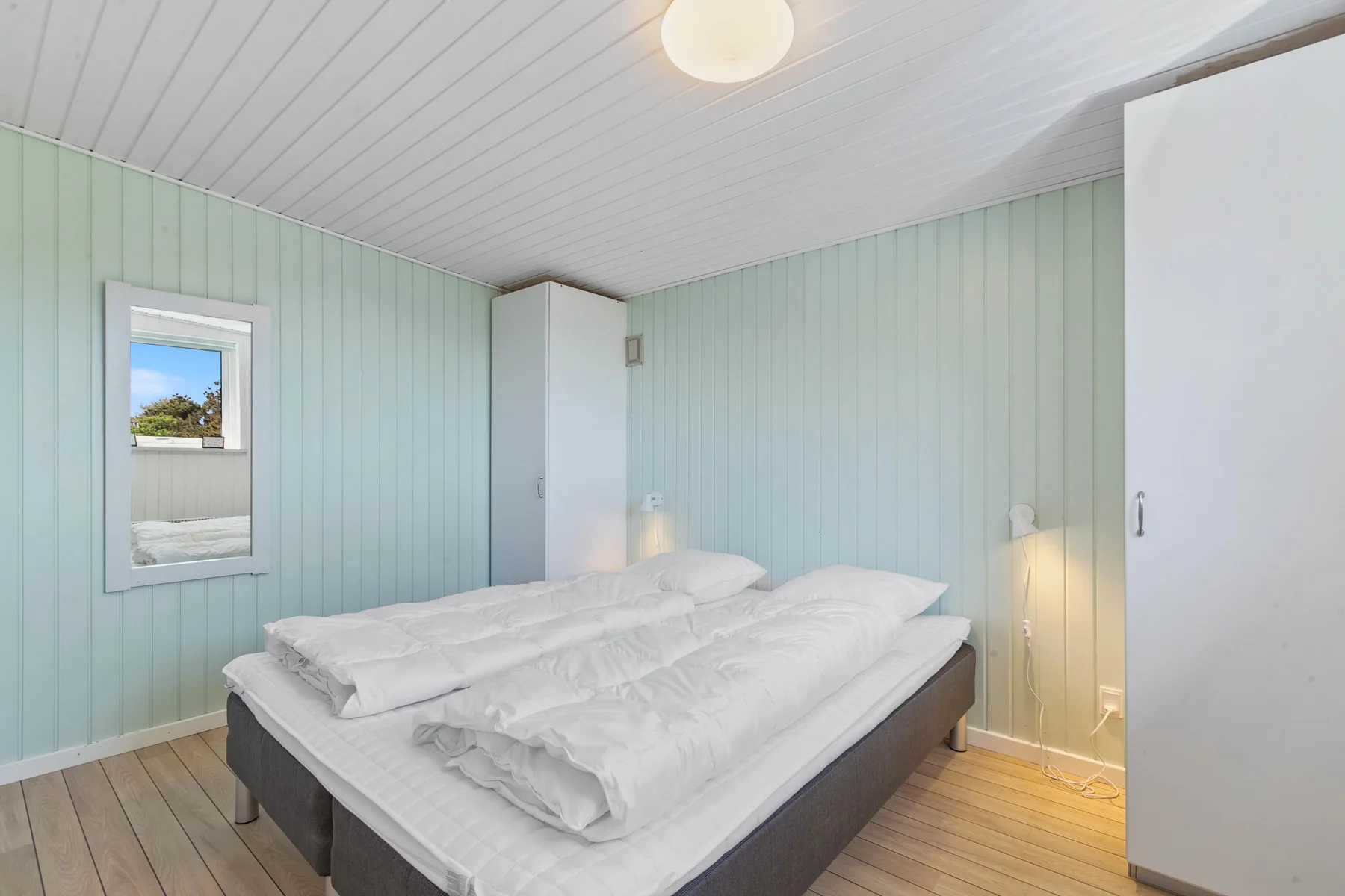 Un dormitorio con una cama doble, paredes verde claro y una ventana pequeña.