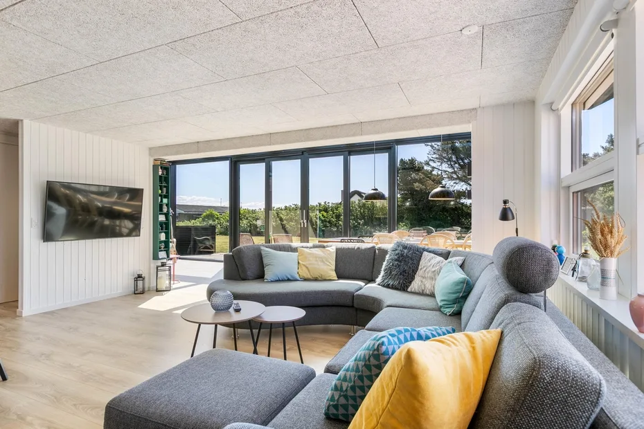 Una sala luminosa con una zona de asientos seccionales y grandes ventanales con vistas a la vegetación.