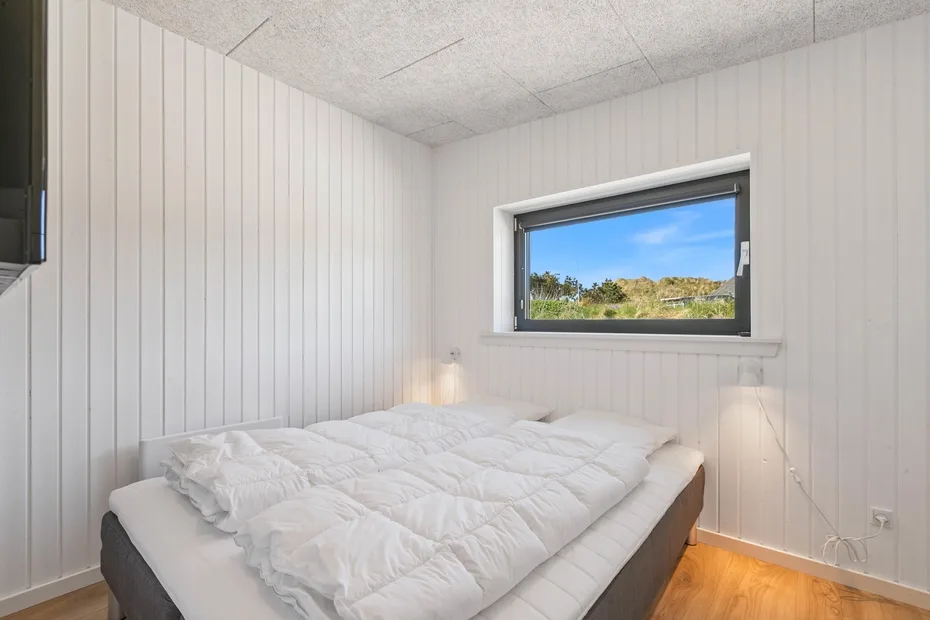 Un dormitorio con una cama bajo una ventana con vistas a la vegetación.