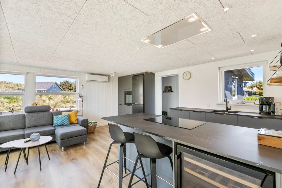 Una cocina y sala de estar diáfanas con un sofá seccional gris y una isla larga.
