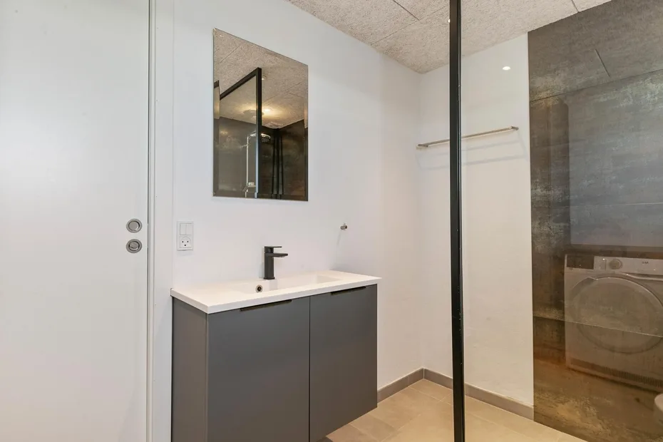 Un baño moderno con tocador, espejo de pared y panel divisorio de vidrio para la ducha.