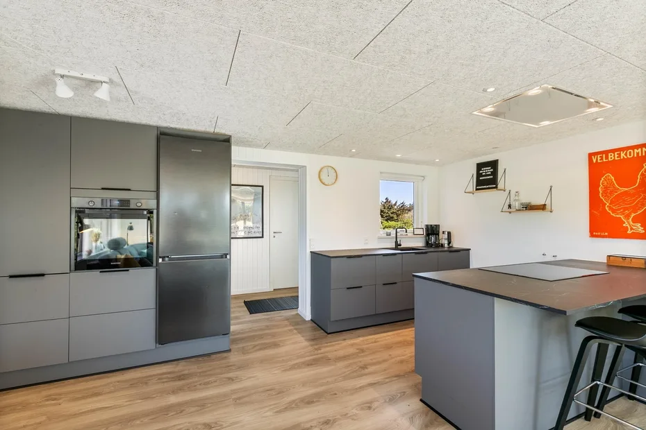 Una cocina moderna con gabinetes grises, una isla central y piso de madera.