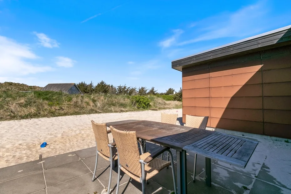 Una zona de comedor en el patio con asientos al aire libre junto a una playa de arena.