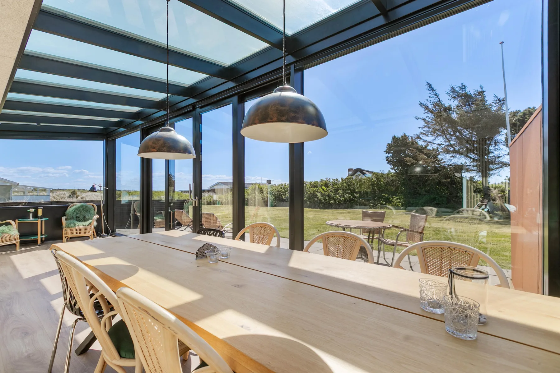 Una mesa de comedor larga está junto a ventanales con vistas al jardín.