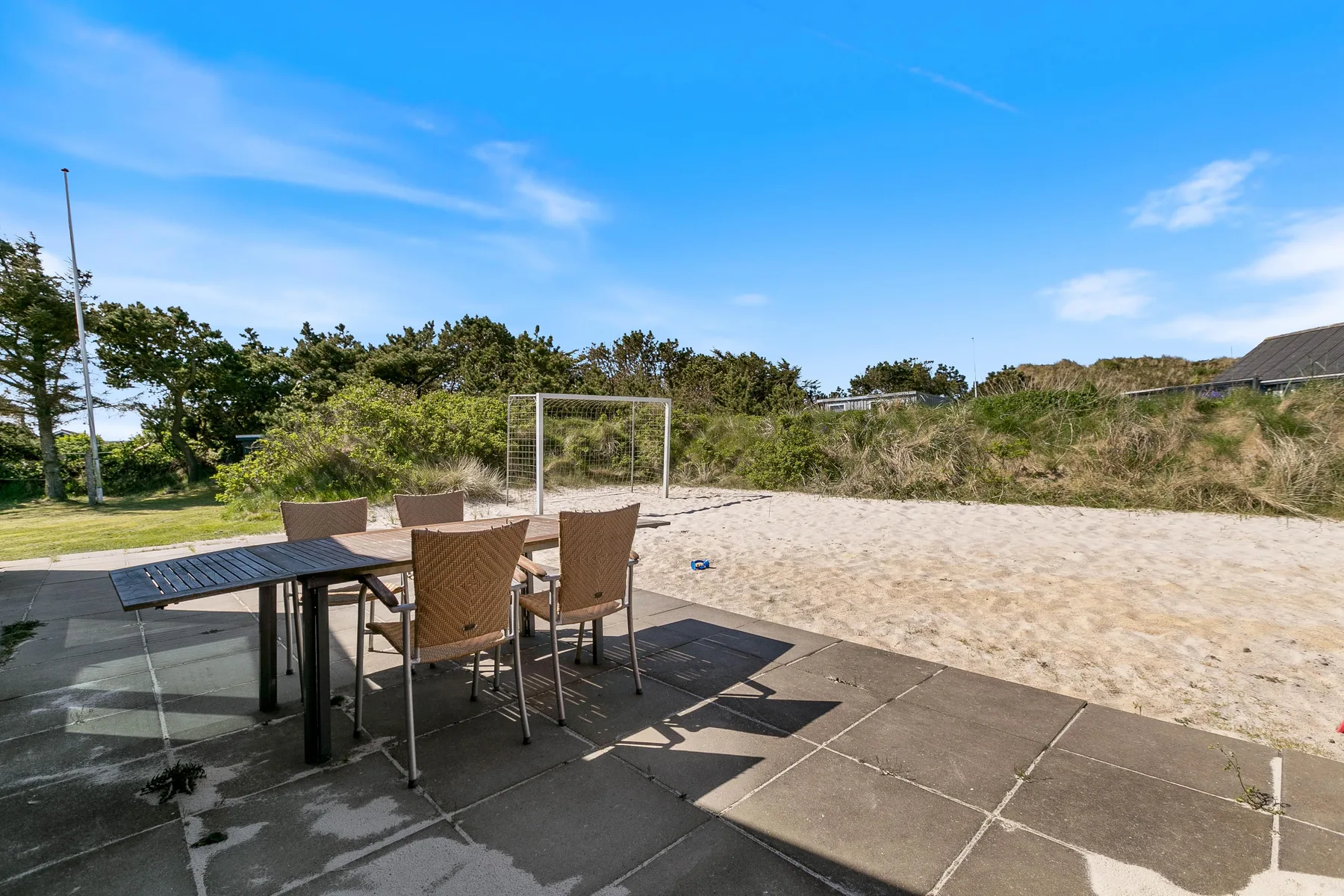 Un patio al aire libre con una mesa y asientos da a una zona arenosa.