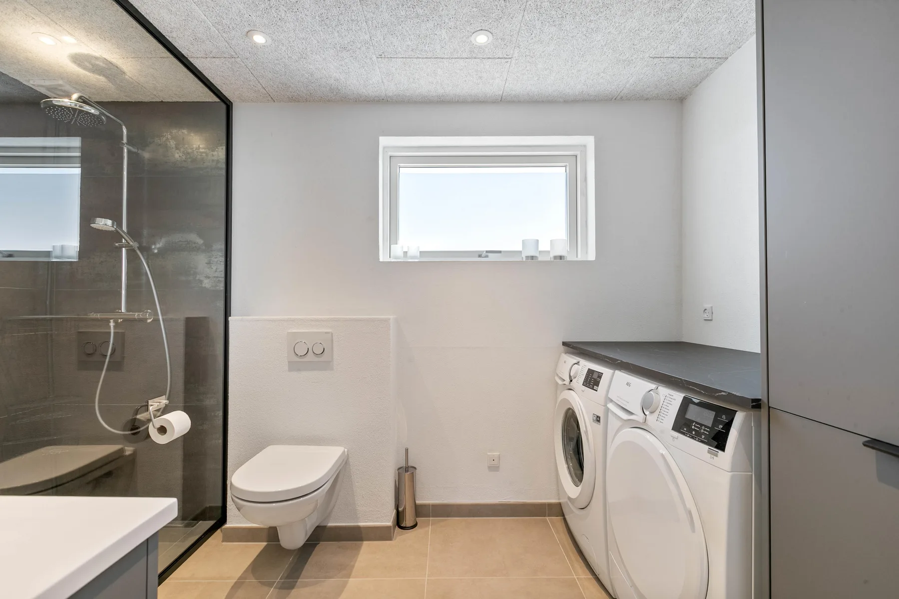 Un baño con ducha de vidrio, inodoro y máquinas de lavandería.