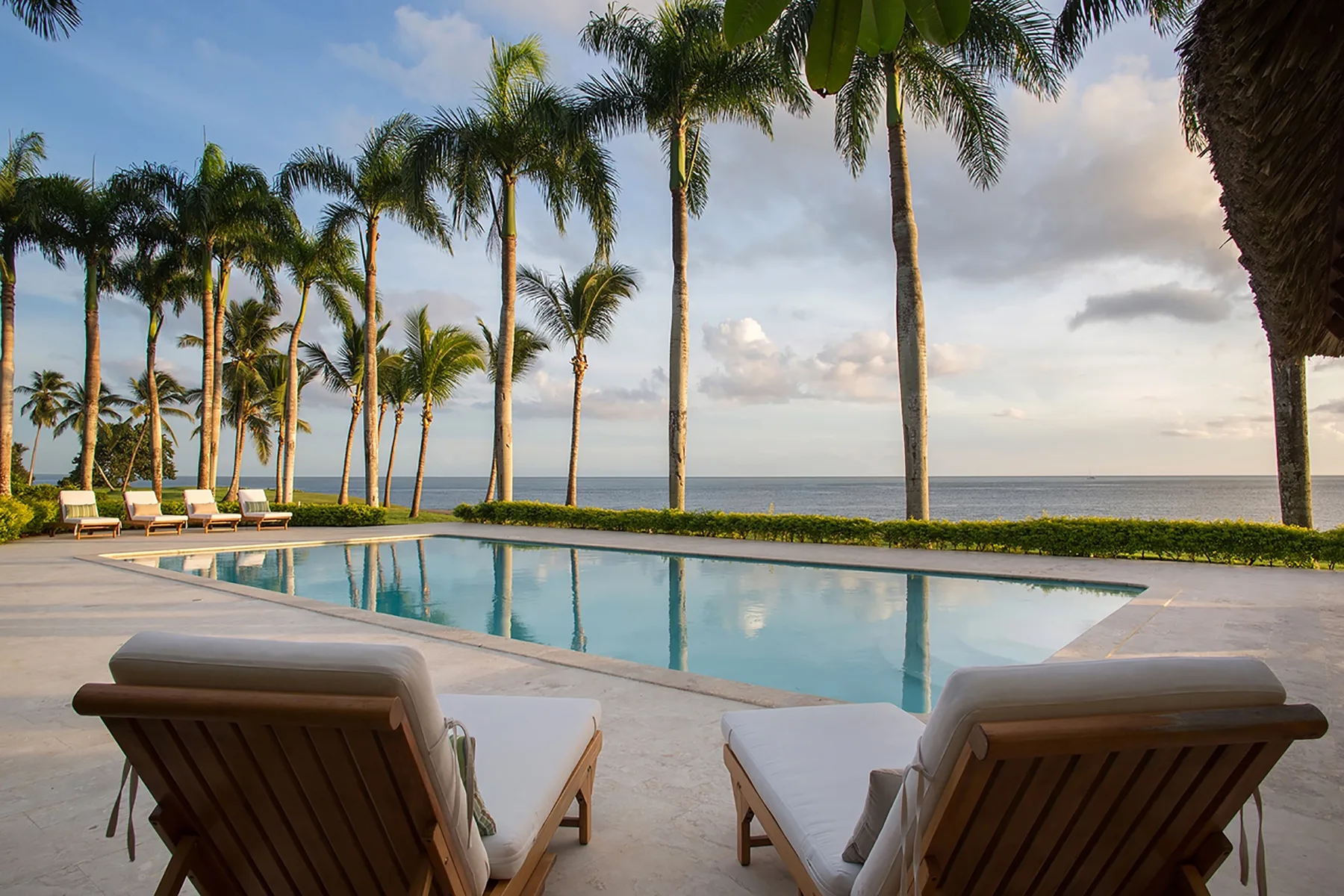 An outdoor pool overlooks the ocean, with lounge seating and palm trees.