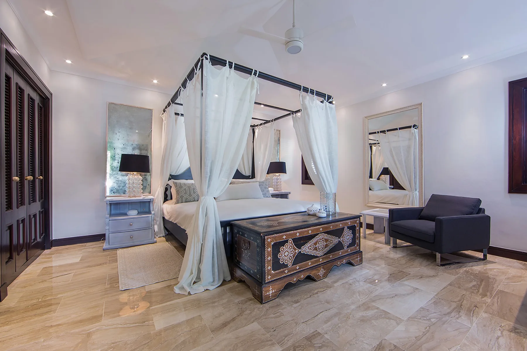 A bedroom with a canopy bed and a dark armchair beside it.