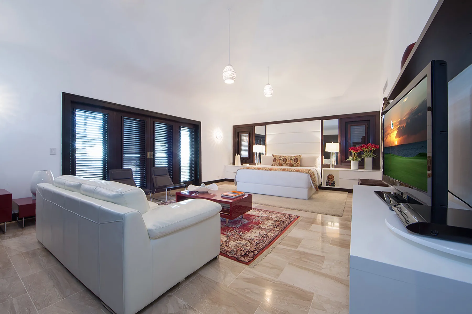 A bright living room with white seating, a rug, and a television.
