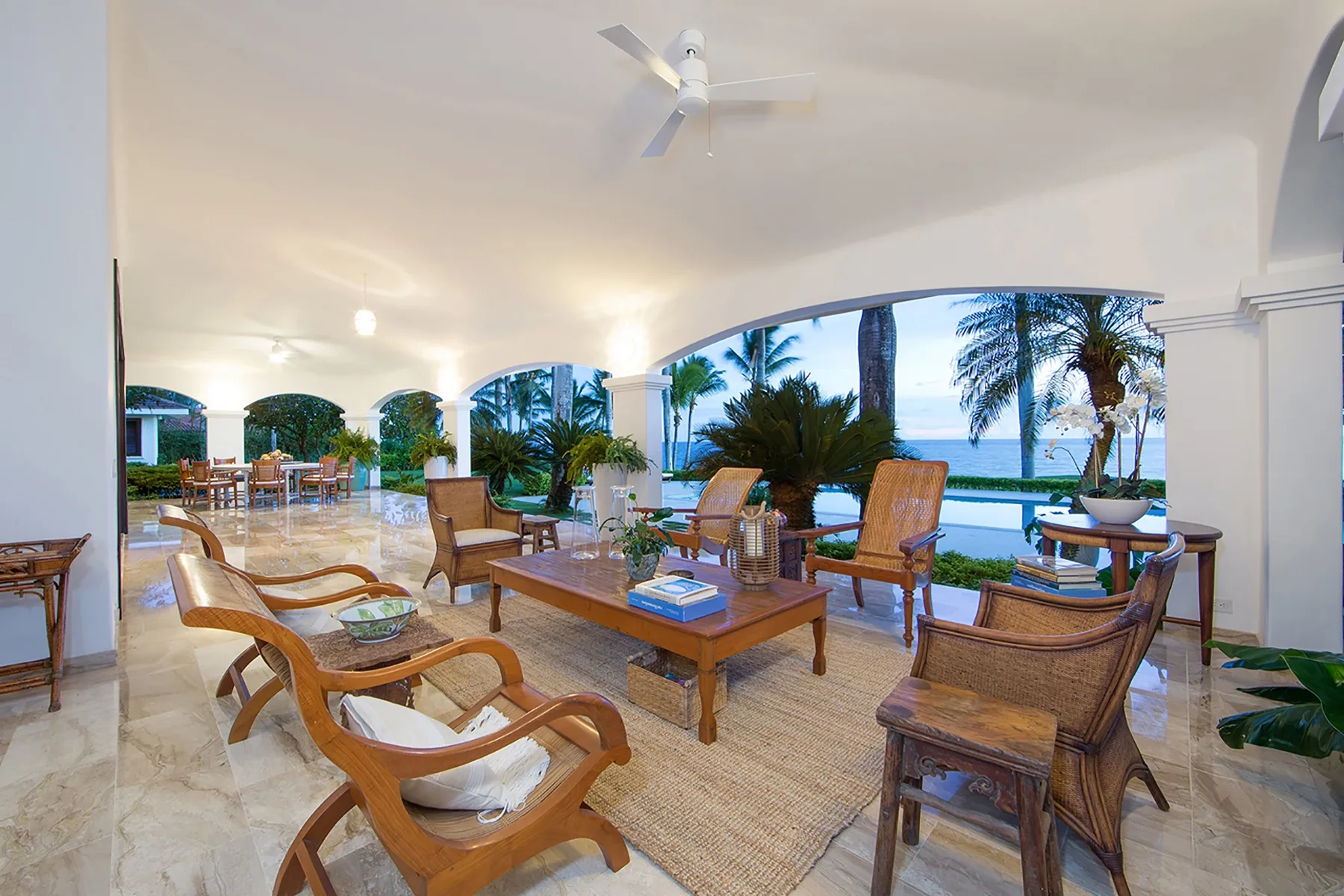 An open lounge with seating and low tables overlooks a garden and pool.