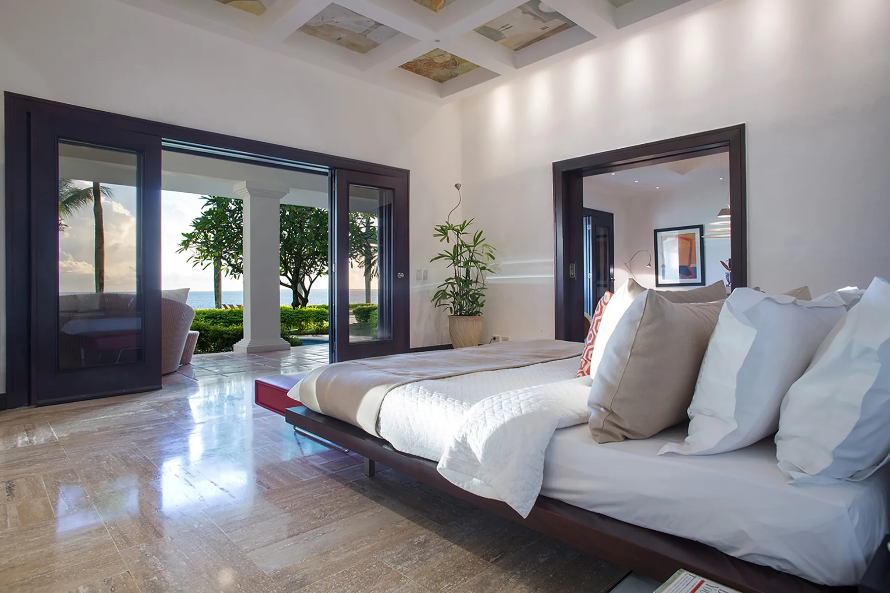A bright bedroom with a bed beside large glass doors opening onto a garden.