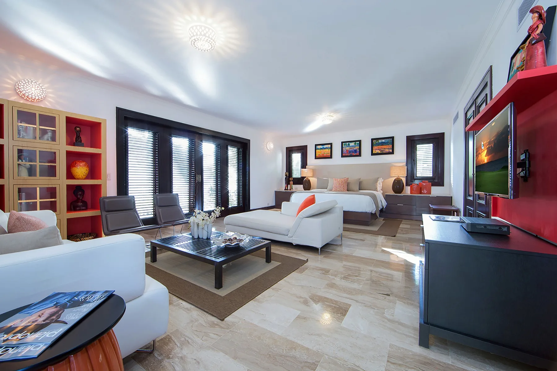 A bright living room with seating, a coffee table, and a bed in the background.