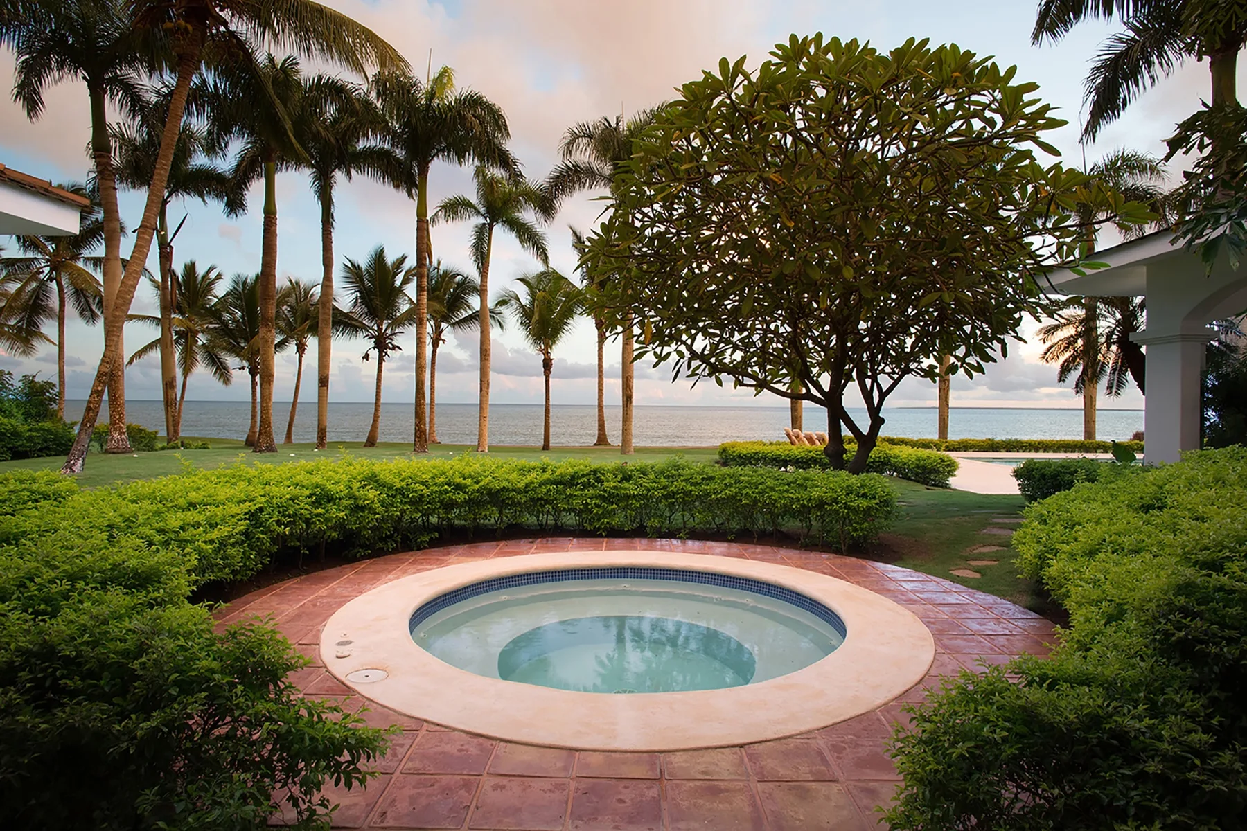 A circular pool sits in a landscaped garden beside the sea.