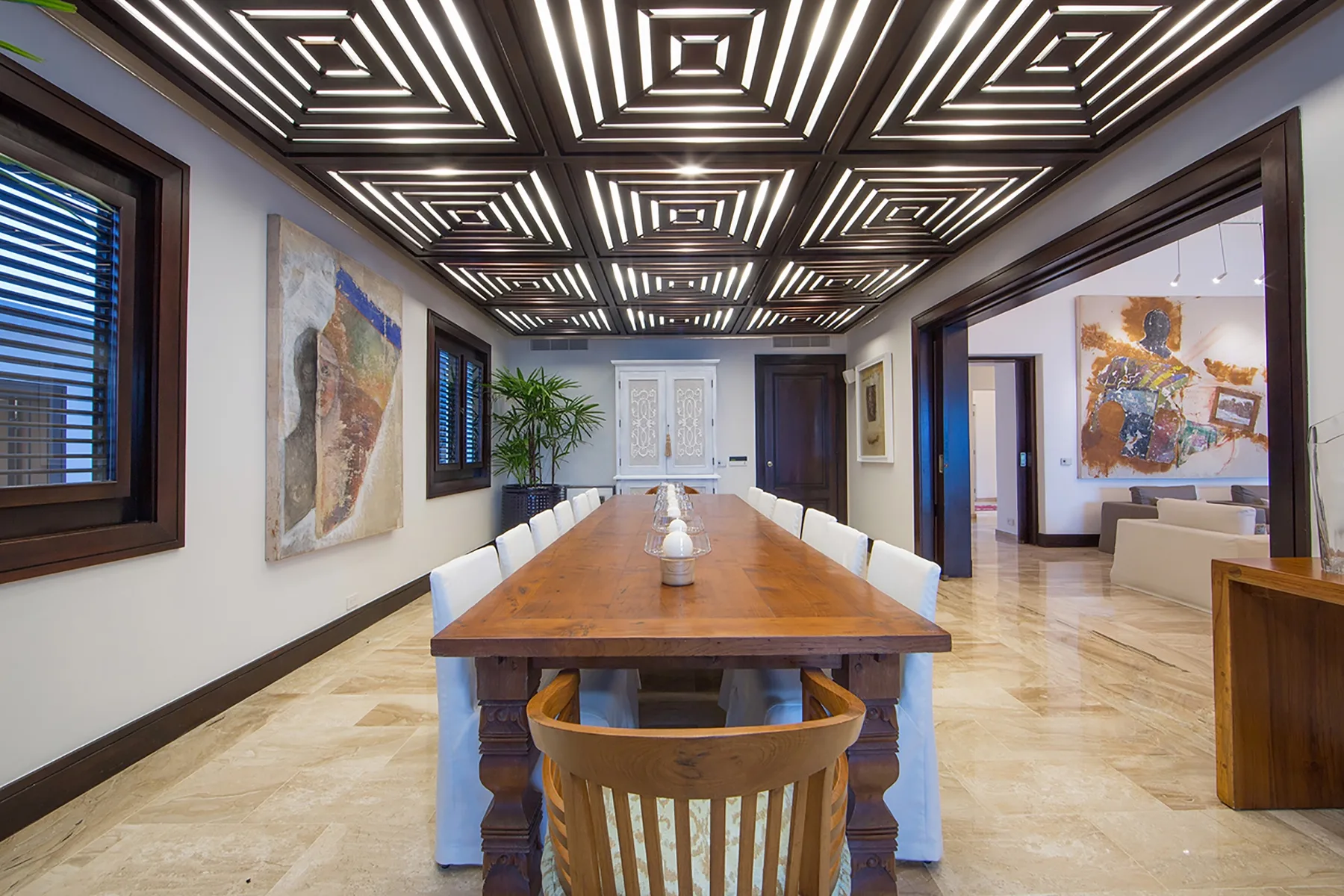 A long dining table sits beneath a patterned ceiling in a spacious interior.