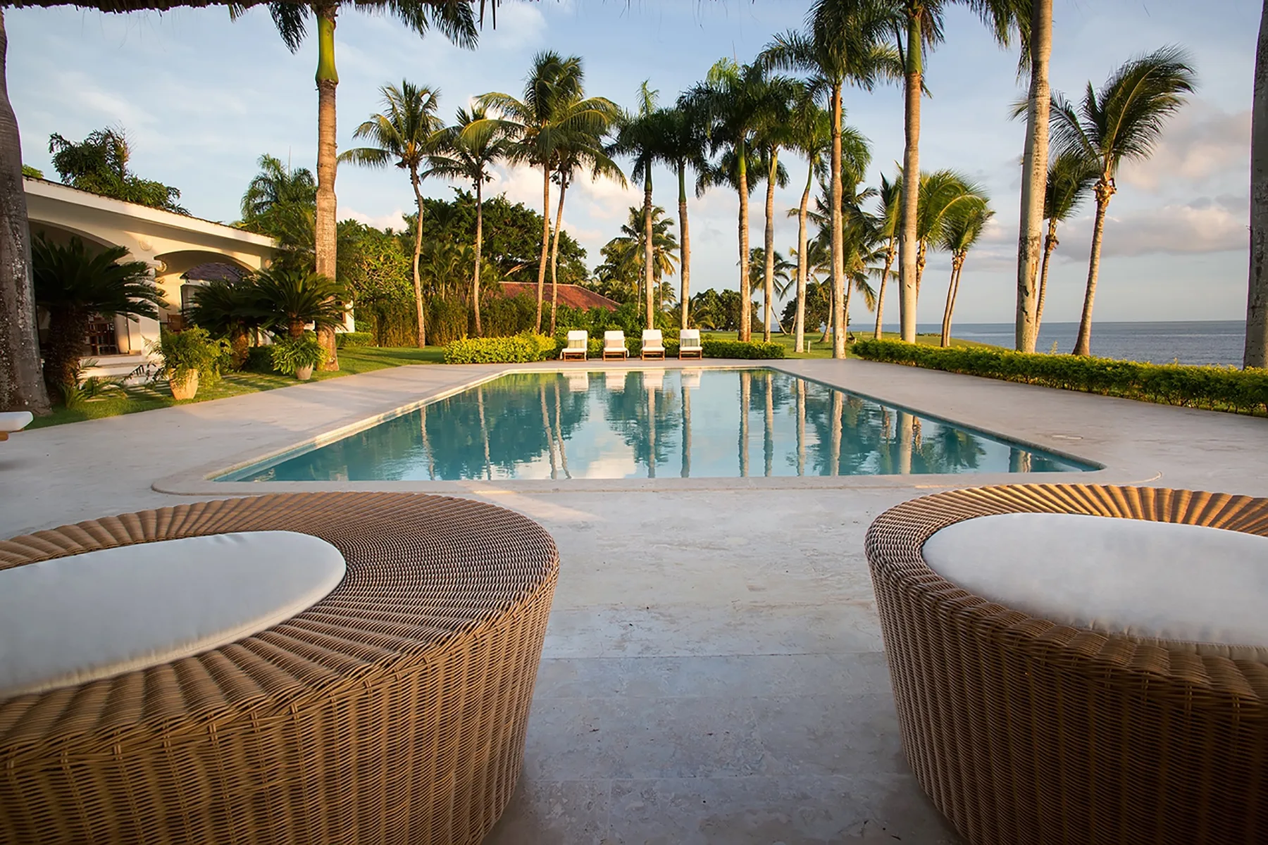 A swimming pool beside palm trees, with the ocean visible beyond.