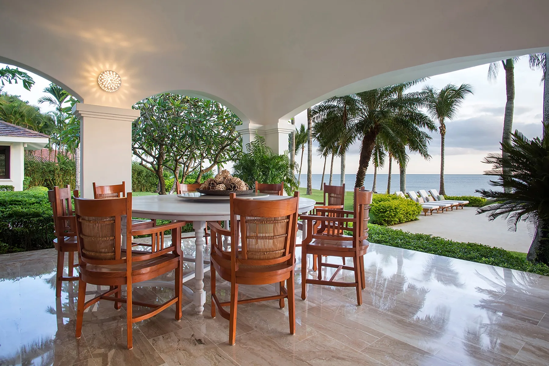 A covered outdoor dining area opens onto a tropical garden and ocean view.