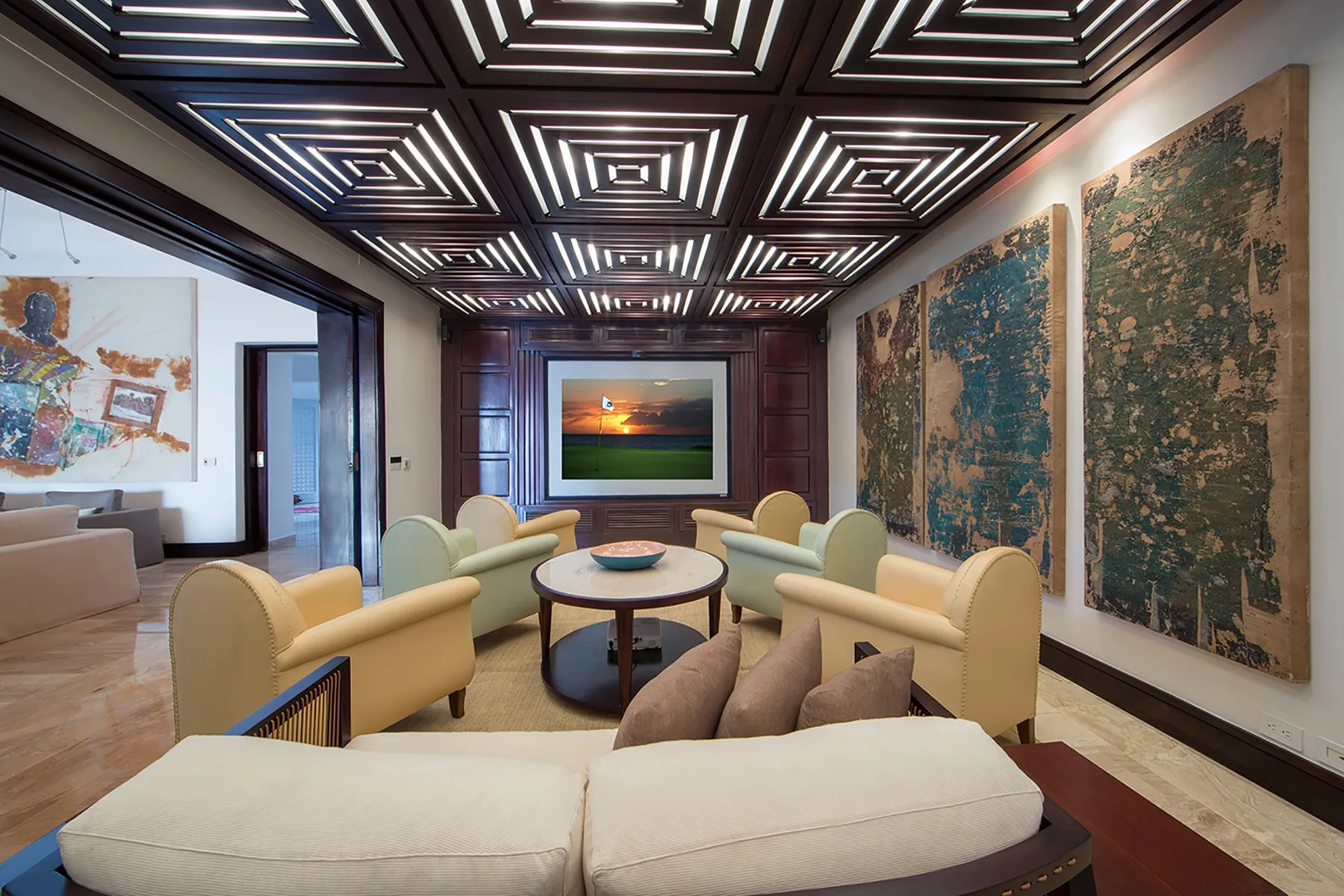 A lounge with pale seating, large wall artworks, and geometric ceiling lights.