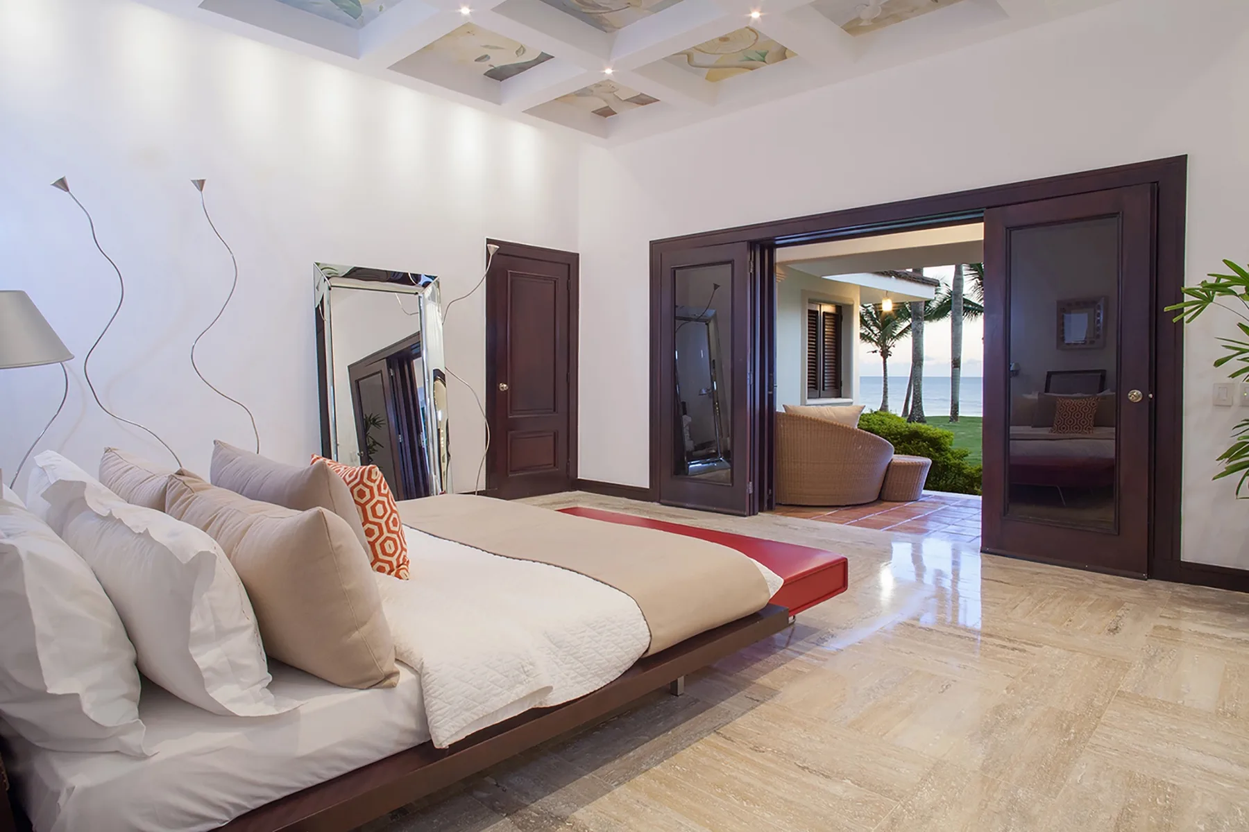 A bright bedroom with a large bed and open doors to an outdoor seating area.