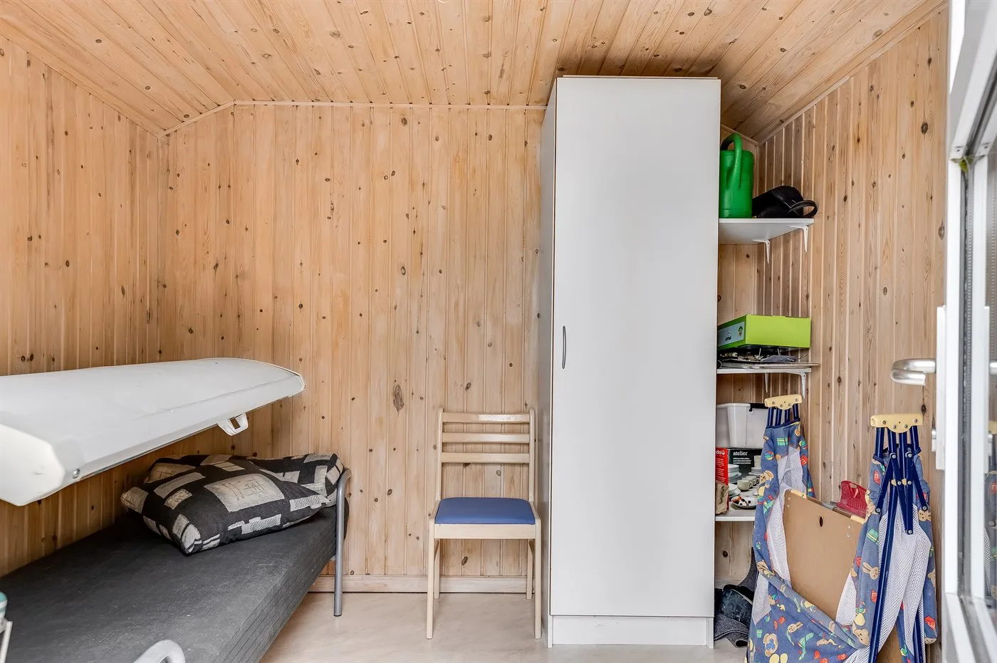 A compact wood-paneled room with a bed, chair, and tall storage cabinet.