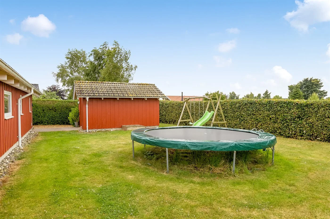A grassy backyard features a trampoline, a swing set, and a red shed.