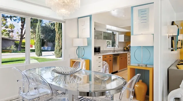 Un comedor luminoso con mesa de vidrio y asientos transparentes se abre a una cocina.