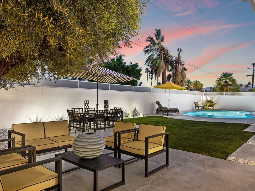 Un patio al aire libre con asientos, una mesa de comedor y una piscina al anochecer.