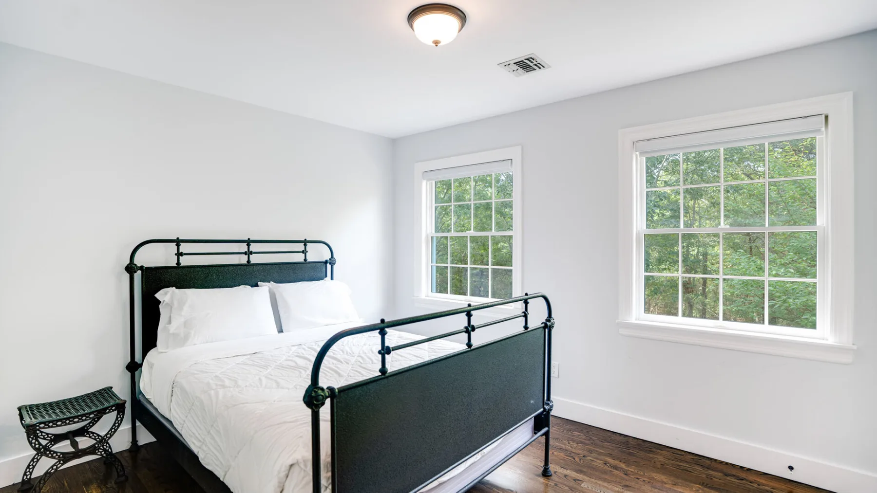 Un dormitorio luminoso con una cama de metal y dos ventanas.