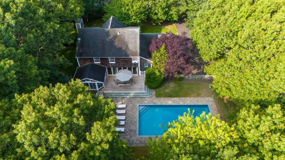 Vista aérea de una casa junto a una piscina, rodeada de árboles.