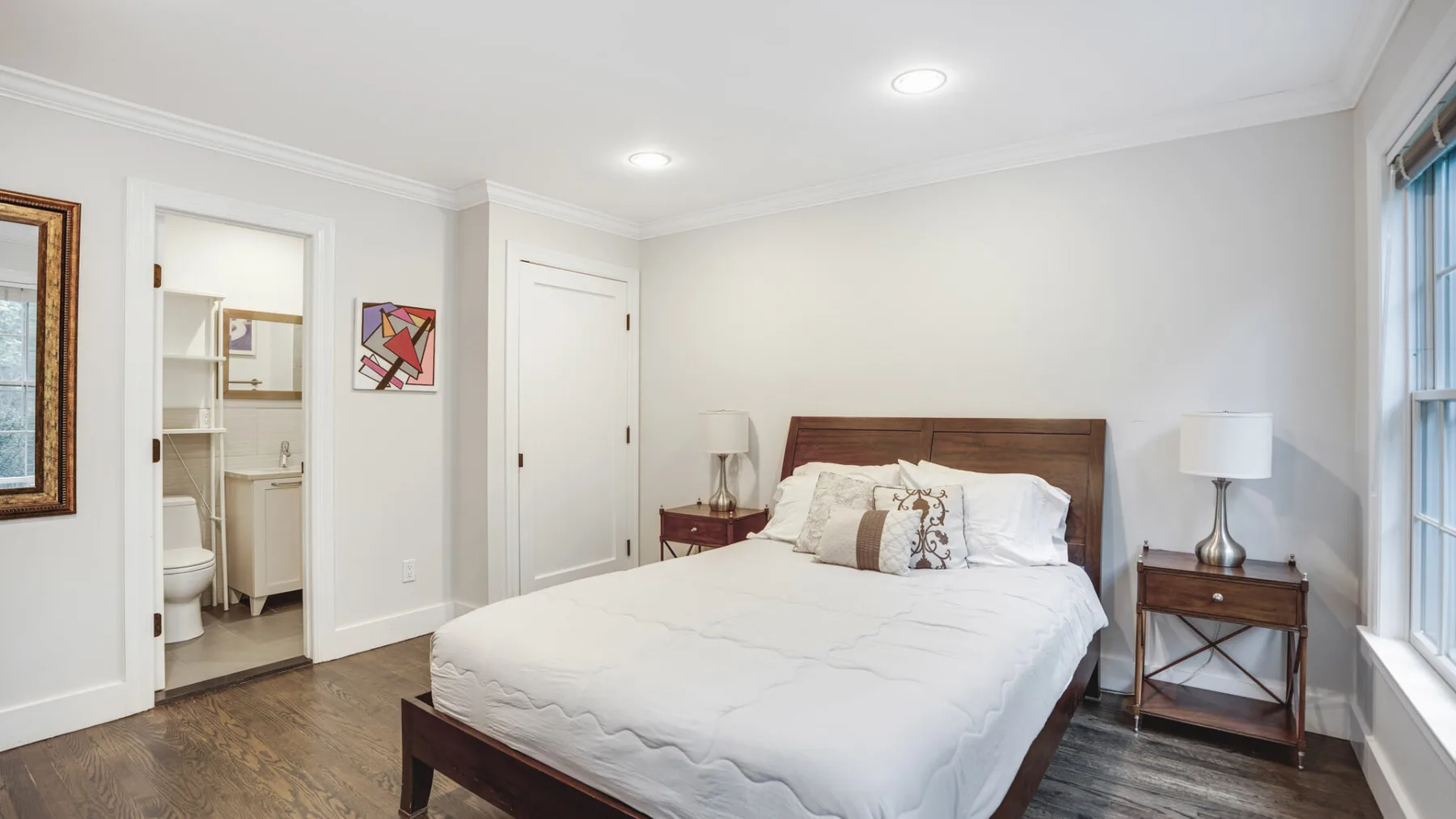 Un dormitorio luminoso con una cama, mesitas de noche y una ventana grande.
