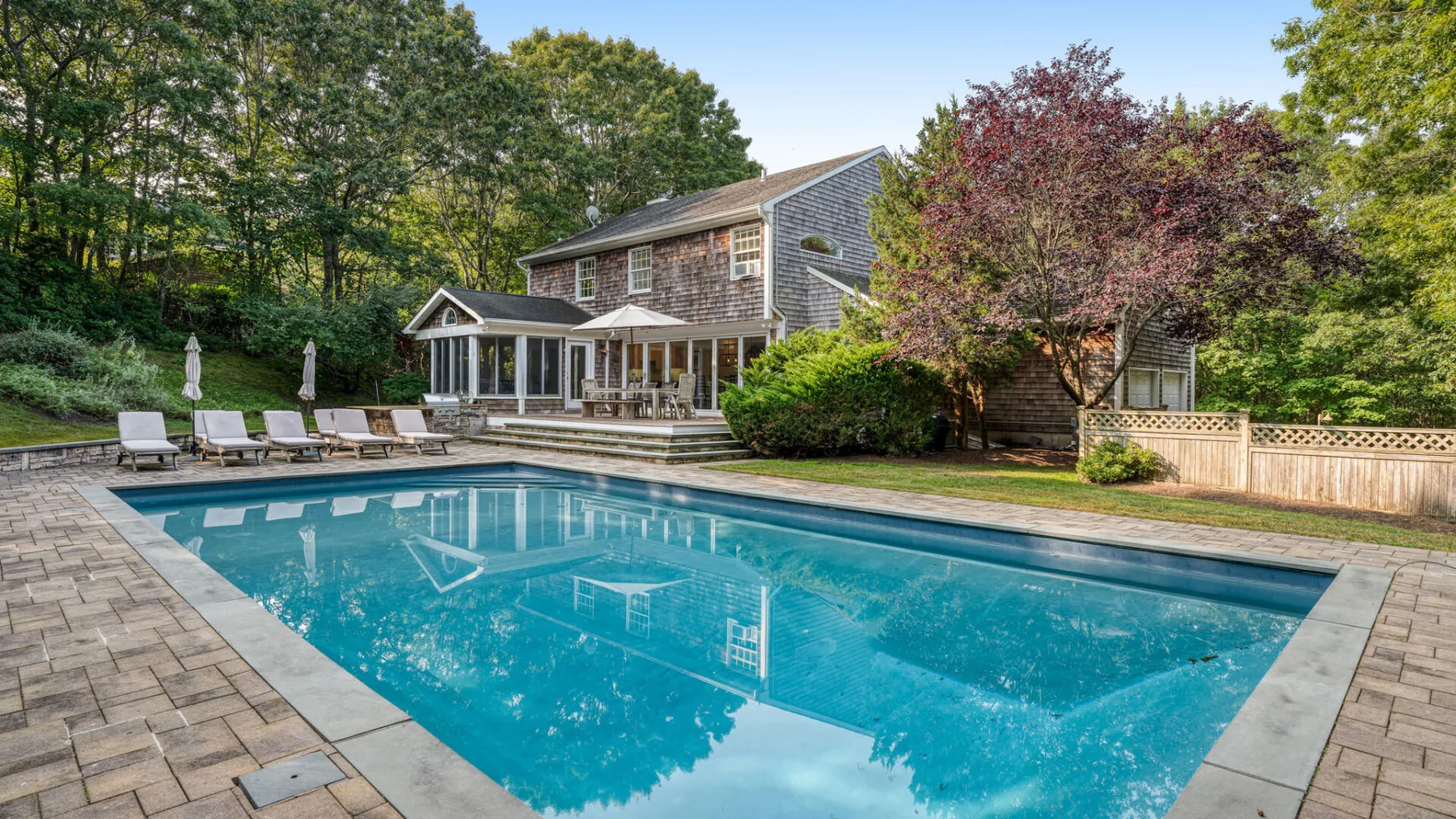 Una piscina exterior está junto a un patio pavimentado y una casa.