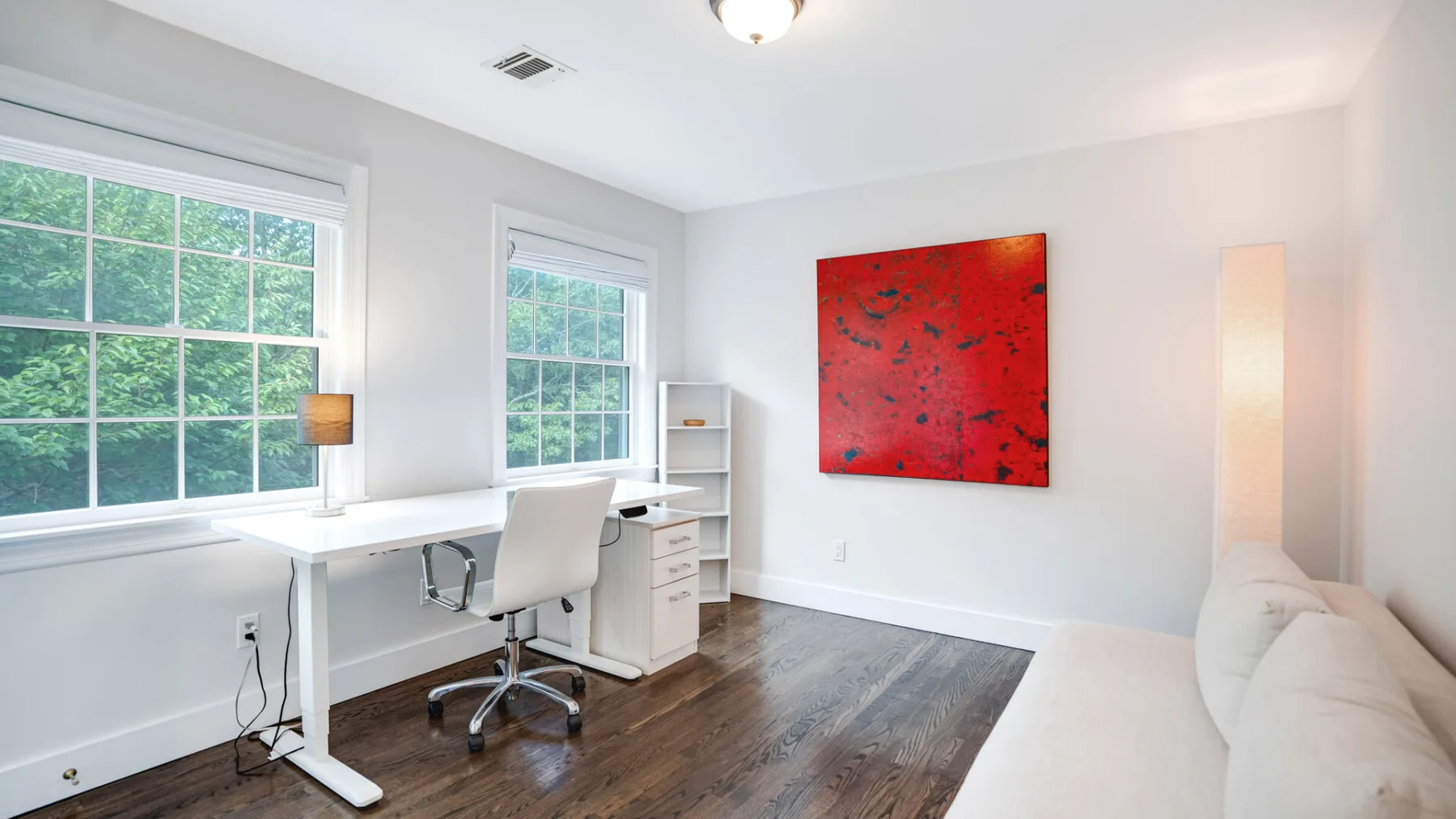 Un despacho luminoso con escritorio, asiento y arte rojo en la pared.
