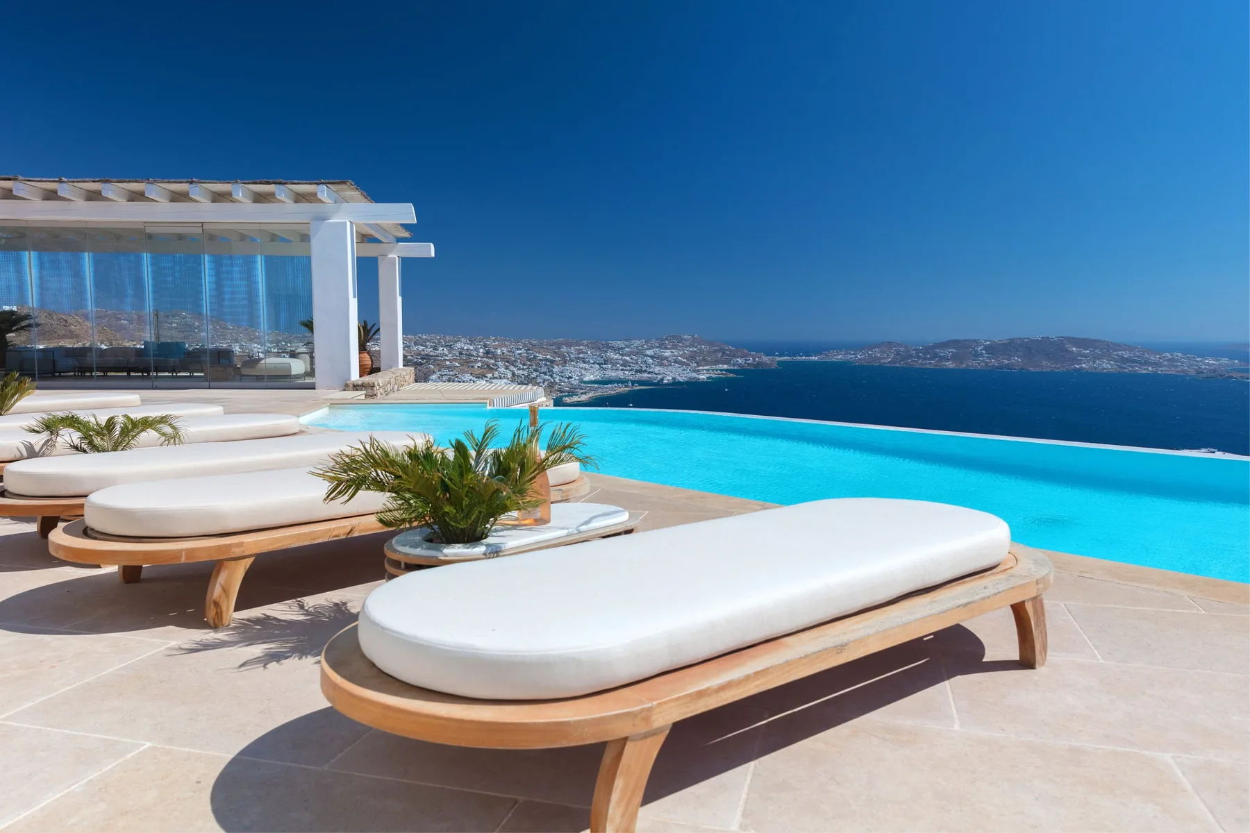 A seaside terrace features a bright swimming pool and cushioned loungers.