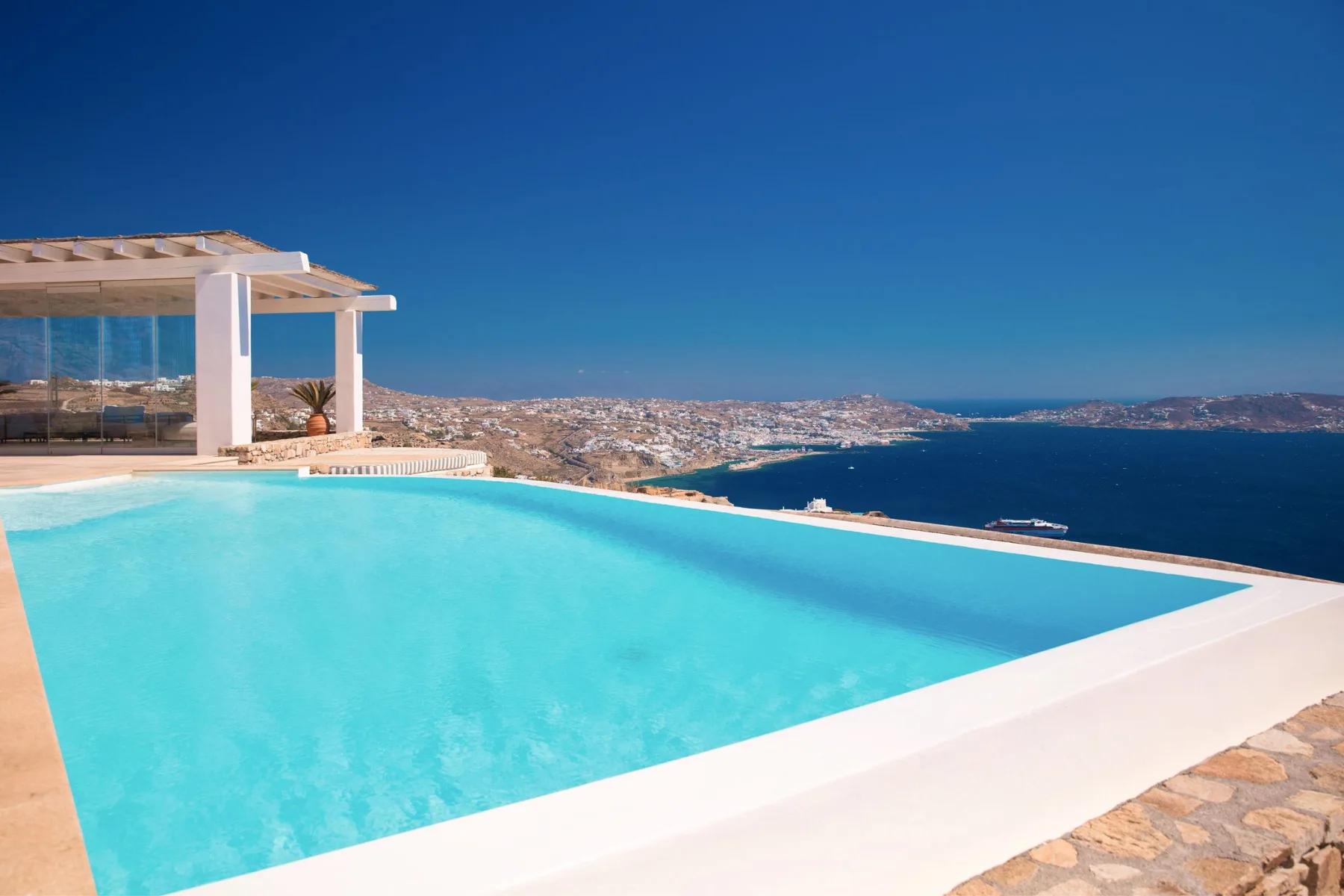 An infinity pool overlooks a coastal town and the sea.