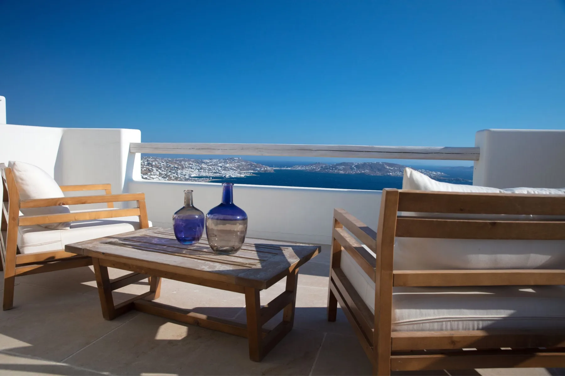 A terrace seating area overlooks the sea, with a low table between the seats.