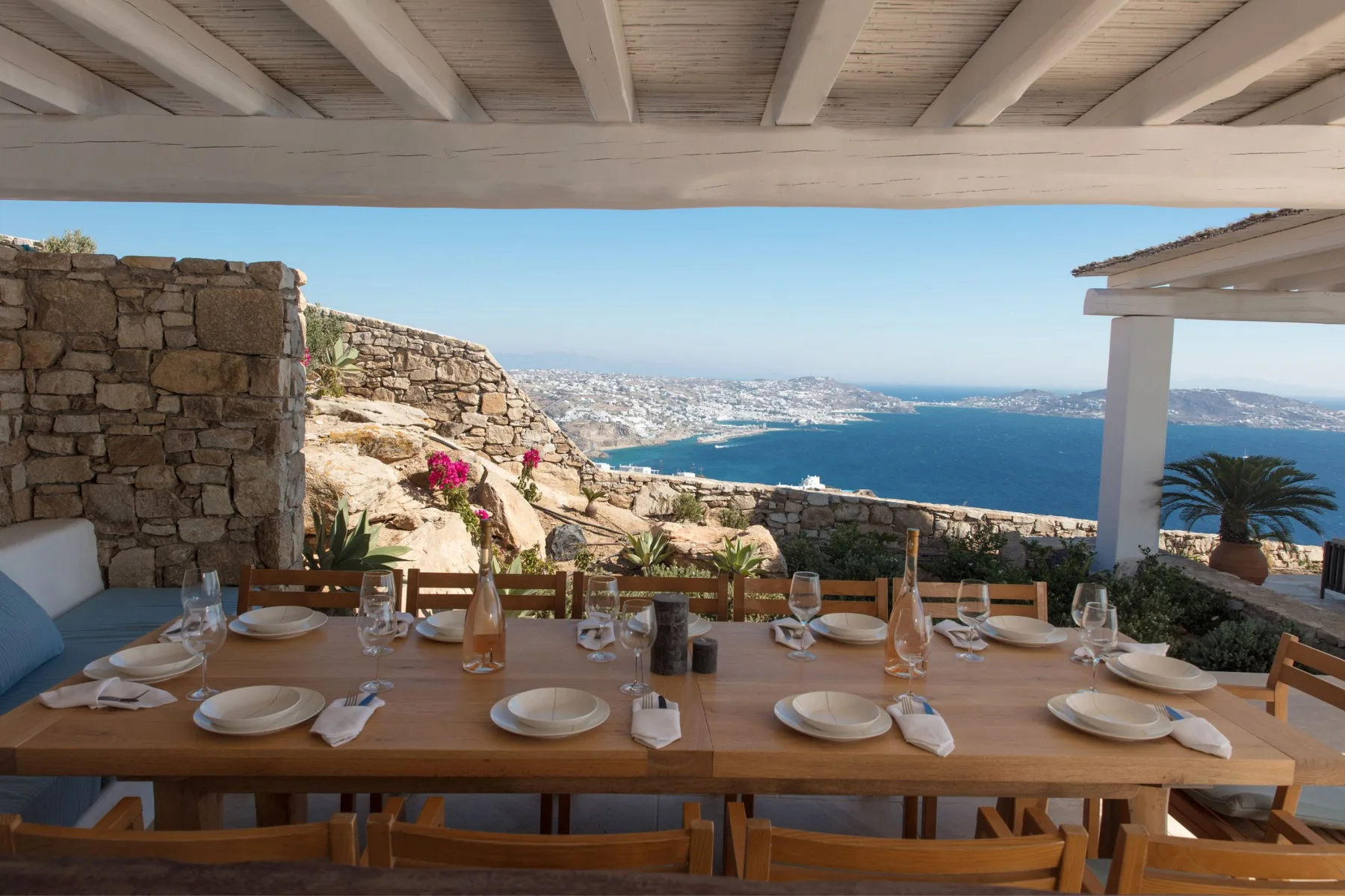 An outdoor dining table overlooks the sea from beneath a covered terrace.